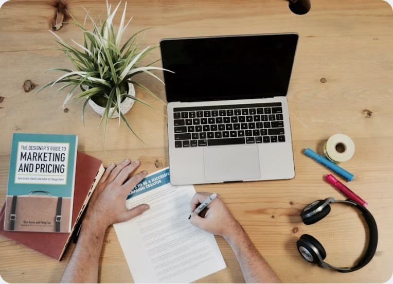 A laptop, notebook and marketing books on a wooden desk