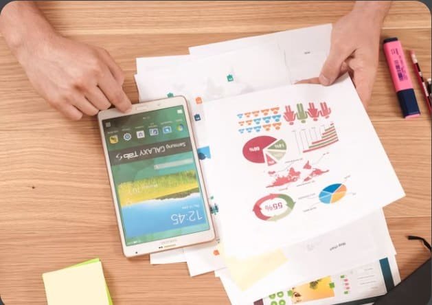 Printed charts and a tablet spread across a desk